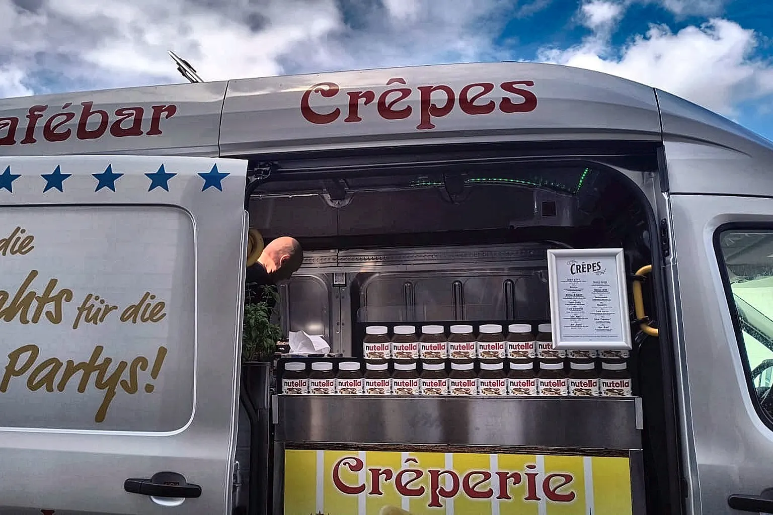 Blick in den geöffneten Crêpes-Wagen mit Backplatte, Aufstrichgläsern und Menütafel.