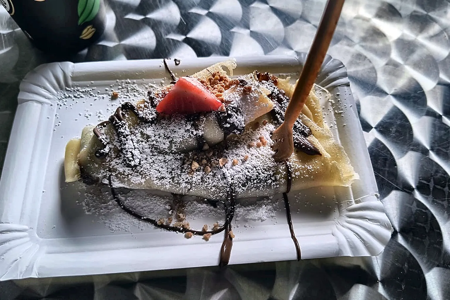 Frisch gebackener Crêpe mit Puderzucker, Schokoladensauce und einer Erdbeere auf einem Teller.